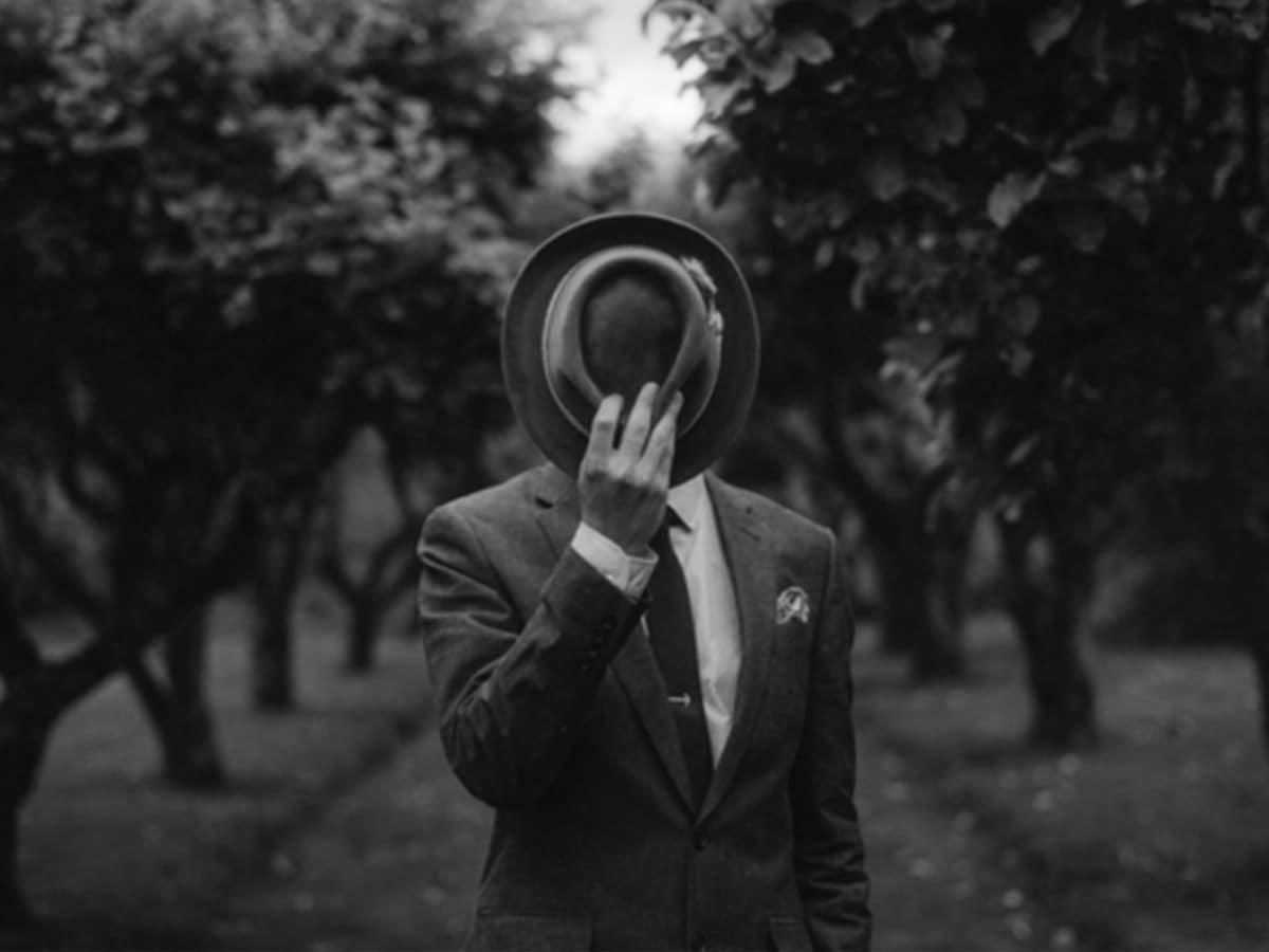 Man in a suit hiding his face with a hat