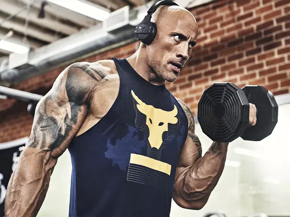 Dwayne Johnson/The Rock wearing headphones and lifting dumbbells