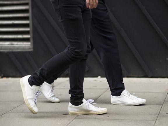 Legs of two men in black jeans and white sneakers