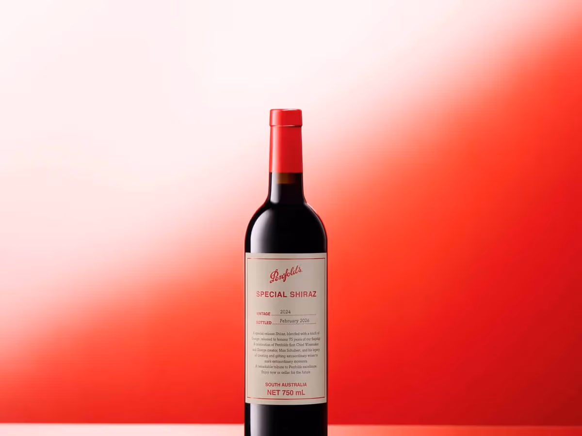 A bottle of Penfolds Special Shiraz 2024 standing on a reflective surface against a graduated red backdrop, with the cream and red label facing forward.