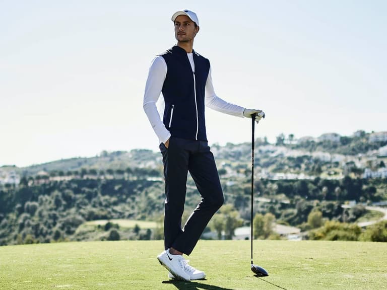 A golfer in a white full-sleeve t-shirt under black sleeveless jacket