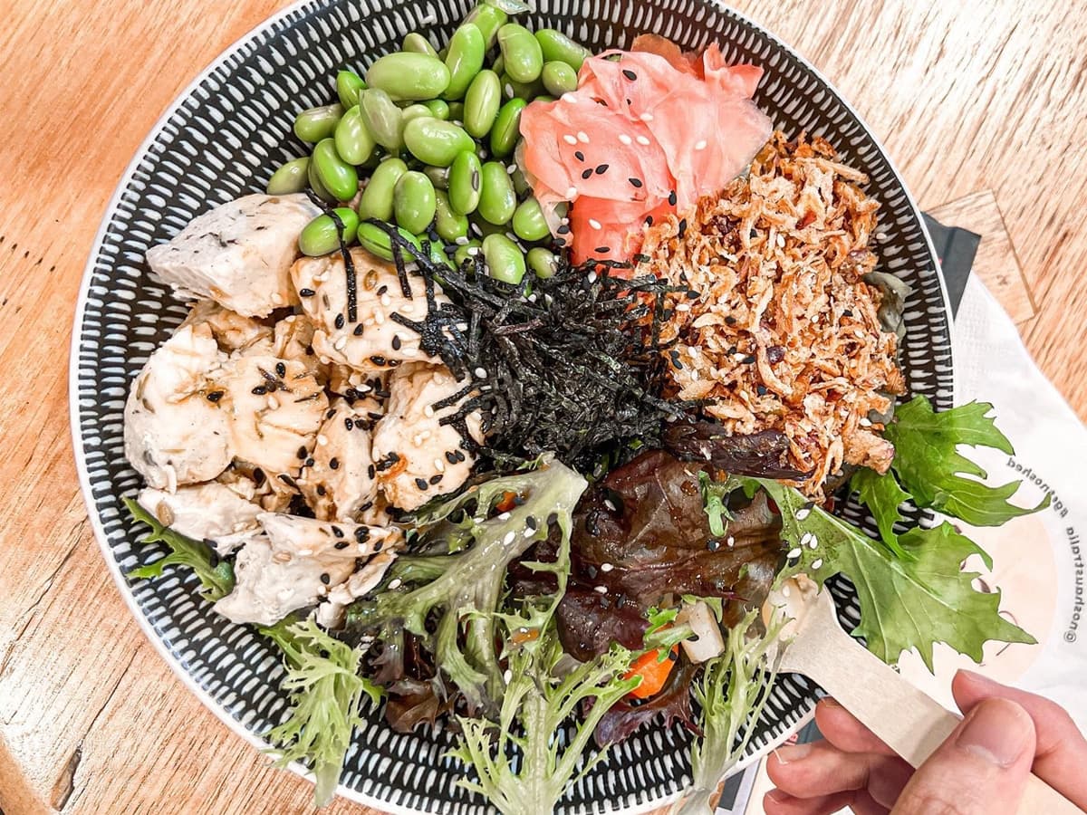 Hand holding a spoonful of poke from one of the two poke bowls on a wooden table
