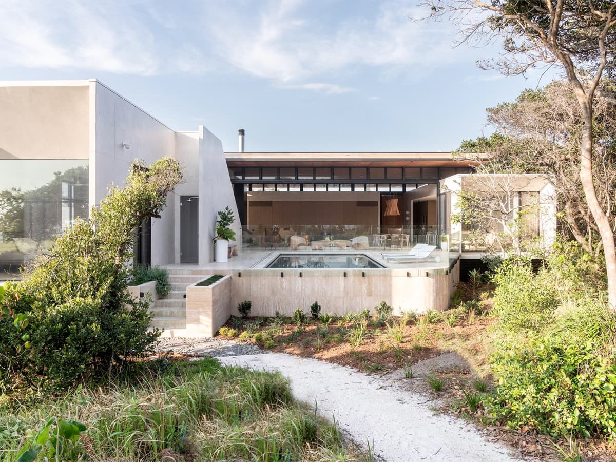 Modern Byron Bay home with expansive glass walls, surrounded by lush greenery and featuring a central pool.