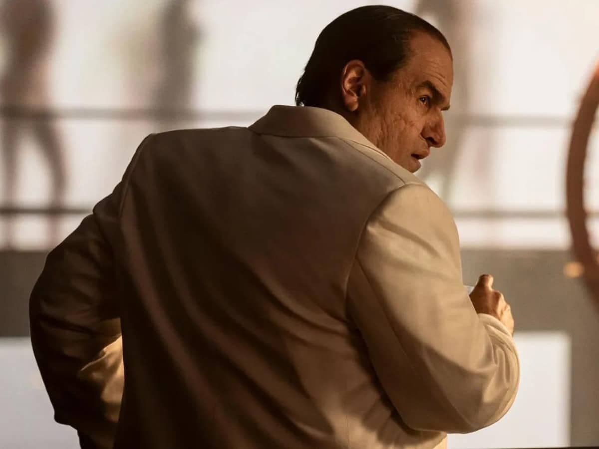 Colin Farrell as The Penguin in a white suit, looking over his shoulder in a dimly lit room.