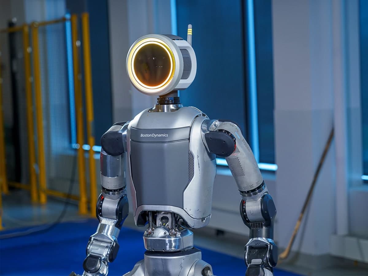 Boston Dynamics Atlas robot with a circular headlight in a well-lit industrial setting.