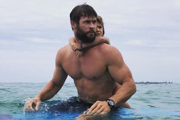 Chris Hemsworth shirtless in water with his child hanging on back