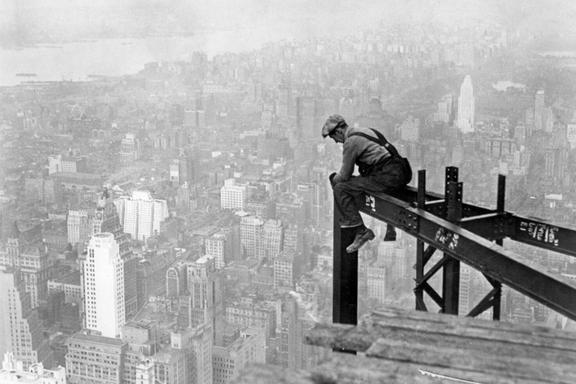 A man working sitting on a steel bar at top of Chrysler Building during construction 