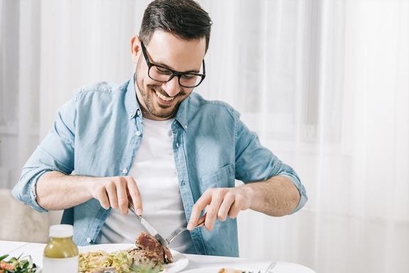 Man smiling and cutting the food on table