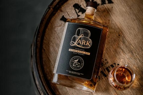 Fallen over bottle of Lark Distilling Co. Symphony No. 1 Whisky on a barrel top next to a glass