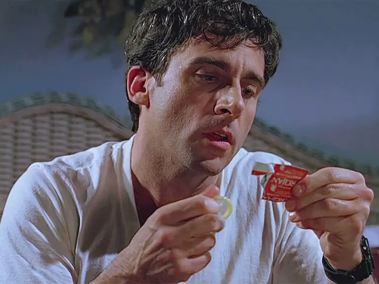 Steve Carrell reading a torn condom packet with a condom in the other hand