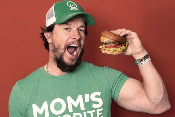 Mark Wahlberg holding a burger near his open mouth