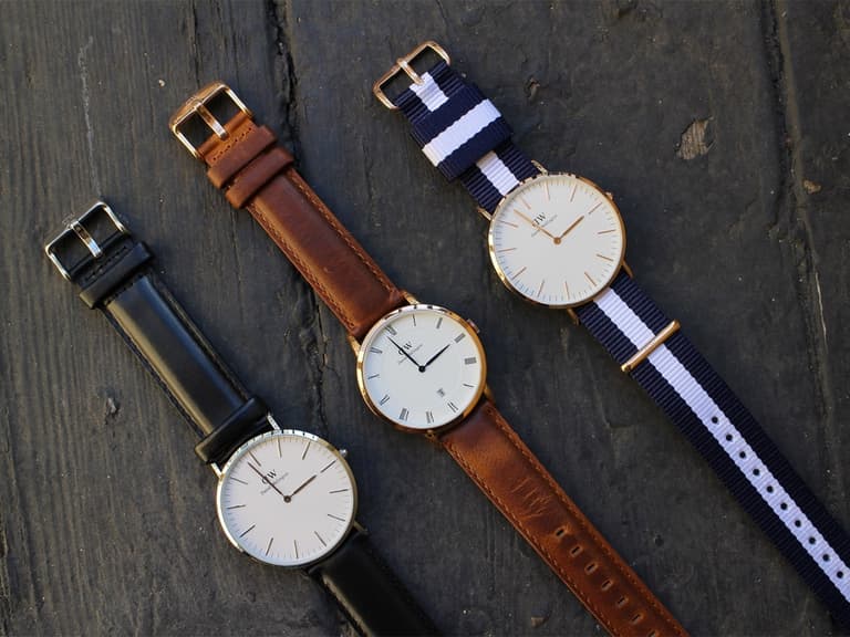Three Daniel Wellington watches on black wood