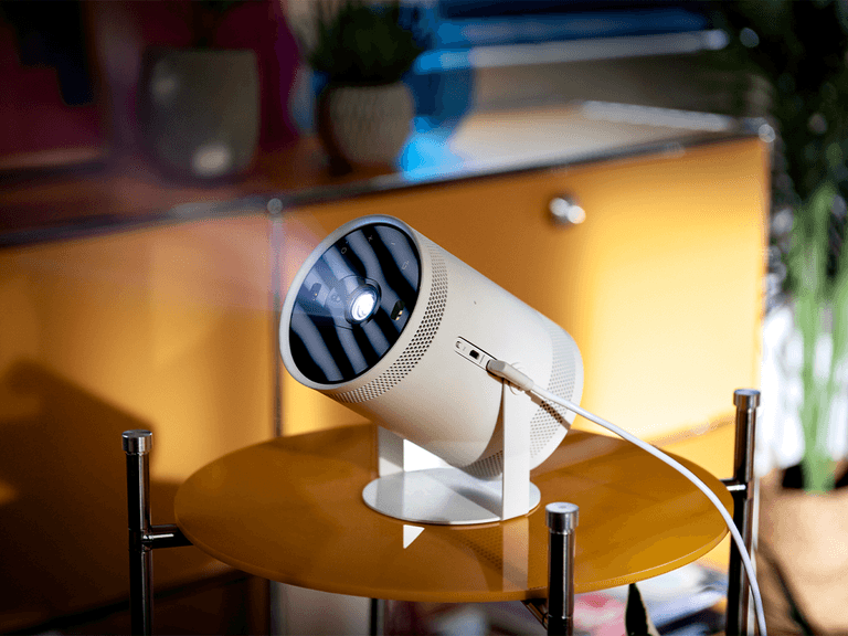 Samsung The Freestyle projector on a yellow table, projecting light in a modern room with vibrant decor.
