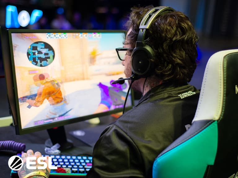 Gamer wearing headphones plays Counter-Strike on a computer at ESL event, seated in a gaming chair.