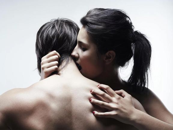 Shirtless woman kissing a shirtless man's neck whose back is facing the camera