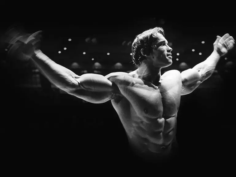 Shirtless Arnold Schwarzenegger raising both arms