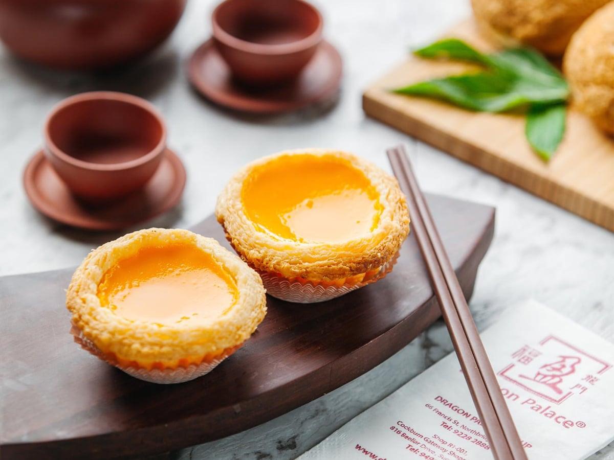 Two egg tarts and chopsticks on a wooden tray