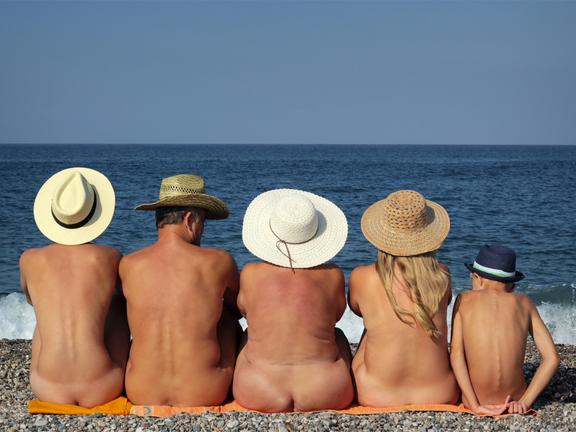 Naked family in hats sitting on the beach