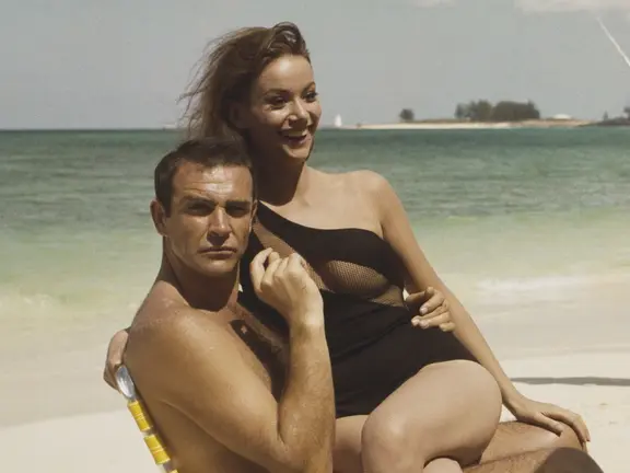 Claudine Auger in a black swimsuit sitting on lap of Sean Connery in a chair