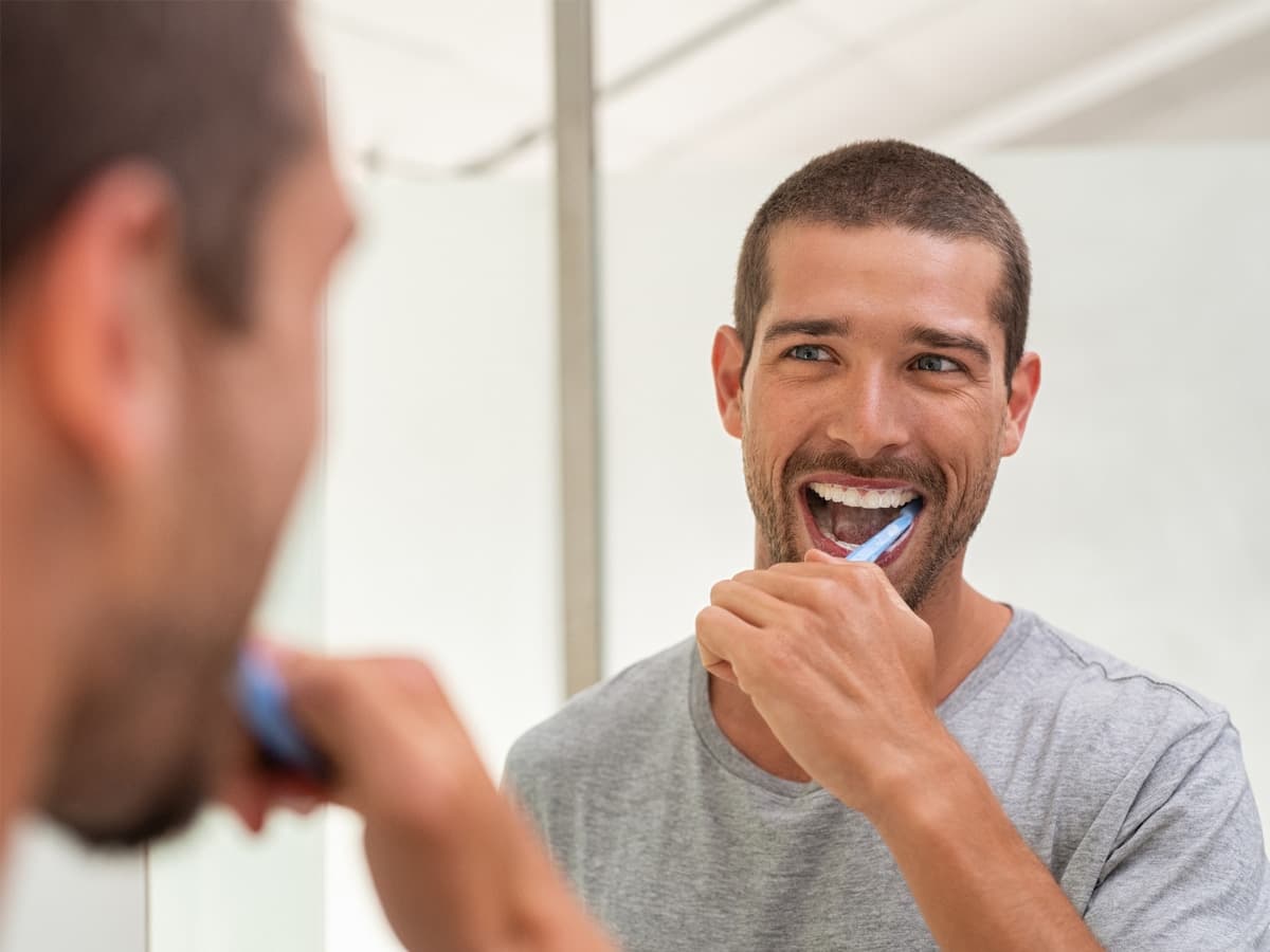man brushing his teeth while looking at himself in the mirror