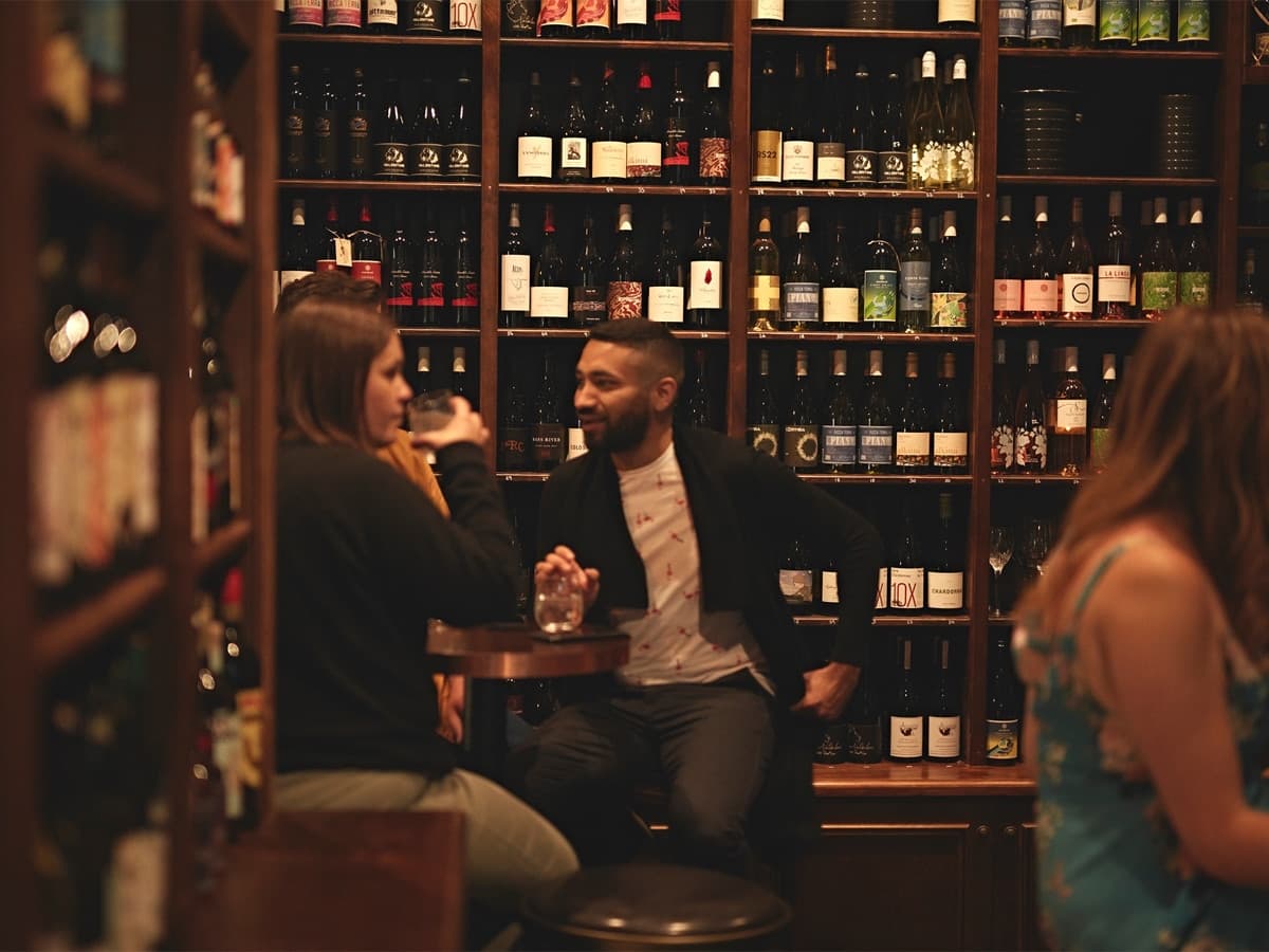 Couple enjoying wine at Bijou Bottle Store bar with shelves of wine bottles in the background.