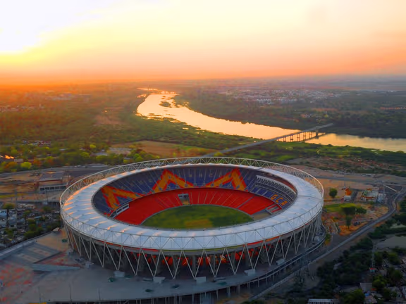Narendra Modi Stadium aerial view at sunset, showcasing its vast seating capacity and surrounding landscape.
