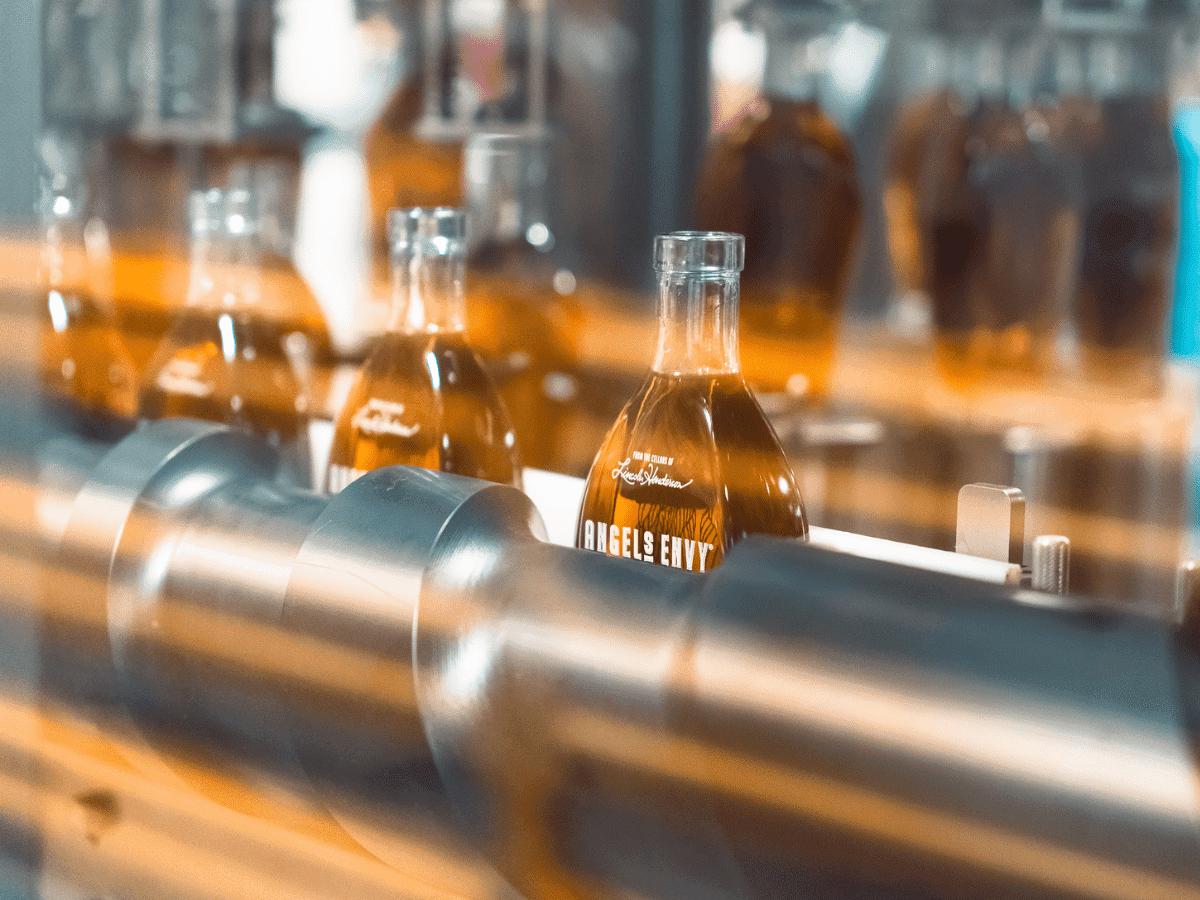 Angel’s Envy bourbon bottles on a production line with warm lighting and blurred motion effect.
