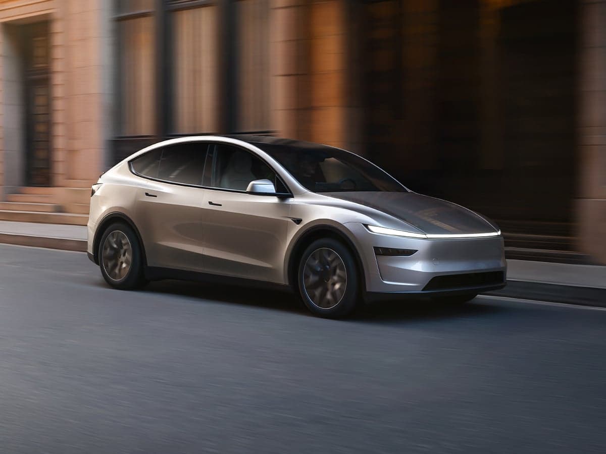 Tesla Model Y L in silver driving on a city street with blurred background and warm lighting.