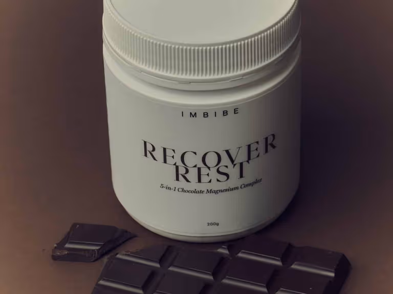IMBIBE RECOVER REST chocolate magnesium tub beside a dark chocolate bar