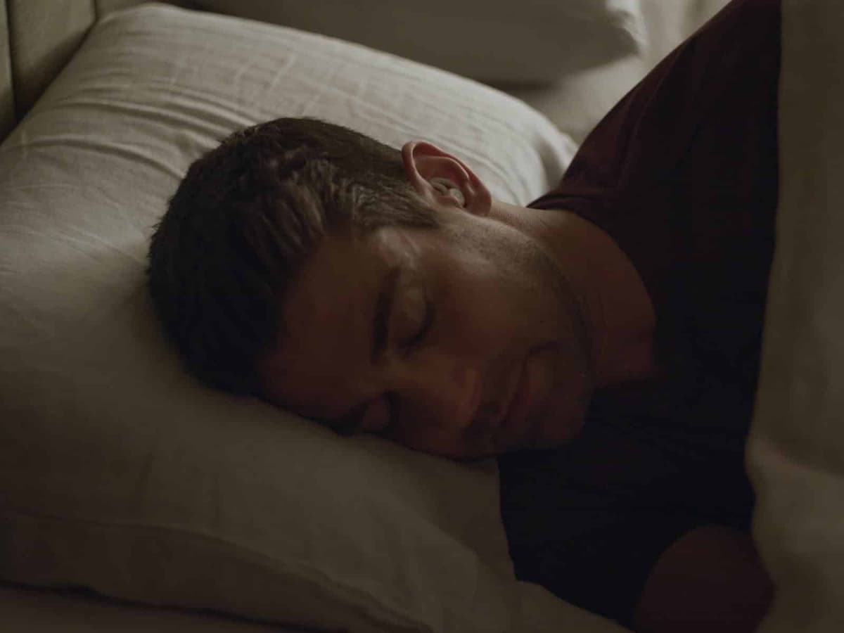 Man sleeping peacefully on his side wearing Ozlo Sleepbuds