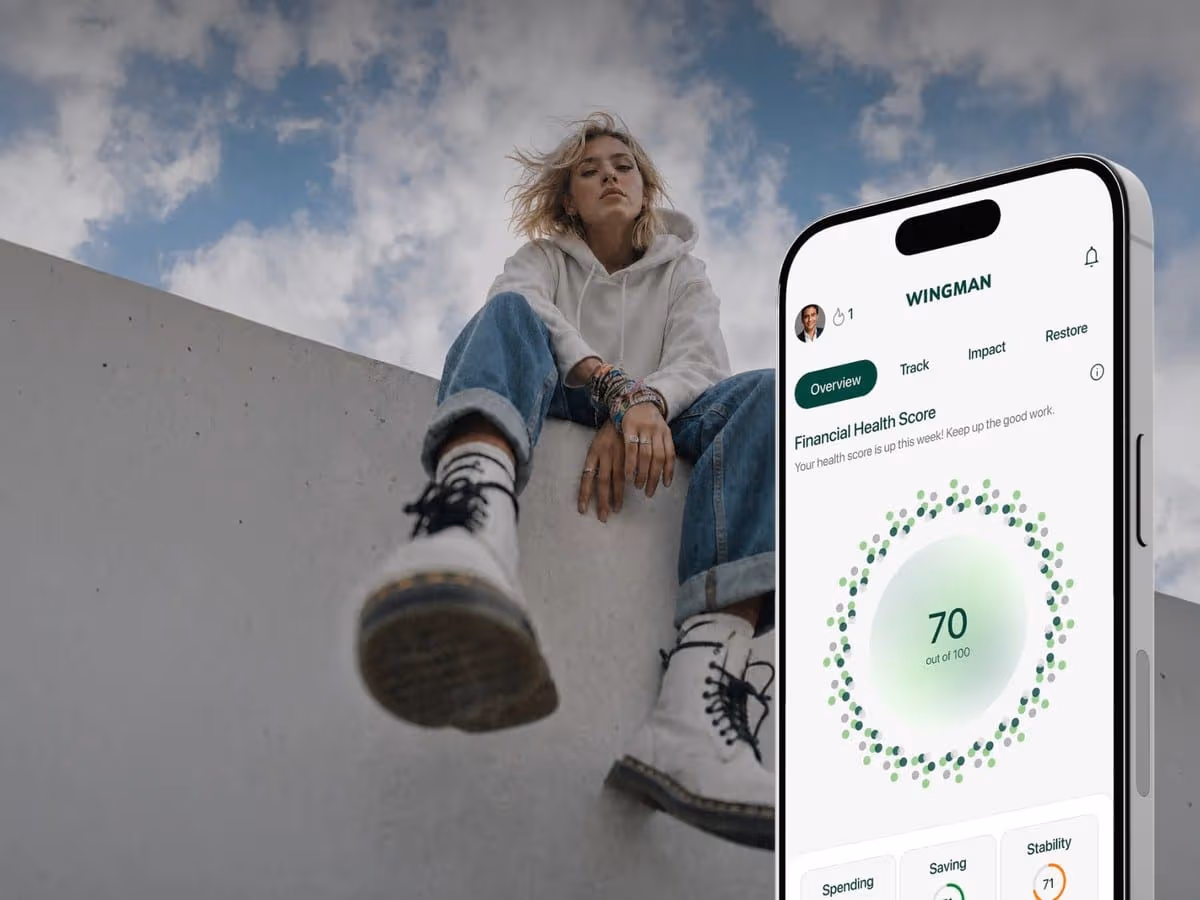 Wingman app showing a Financial Health Score of 70 out of 100 on a phone, with a young woman sitting on a concrete wall behind it
