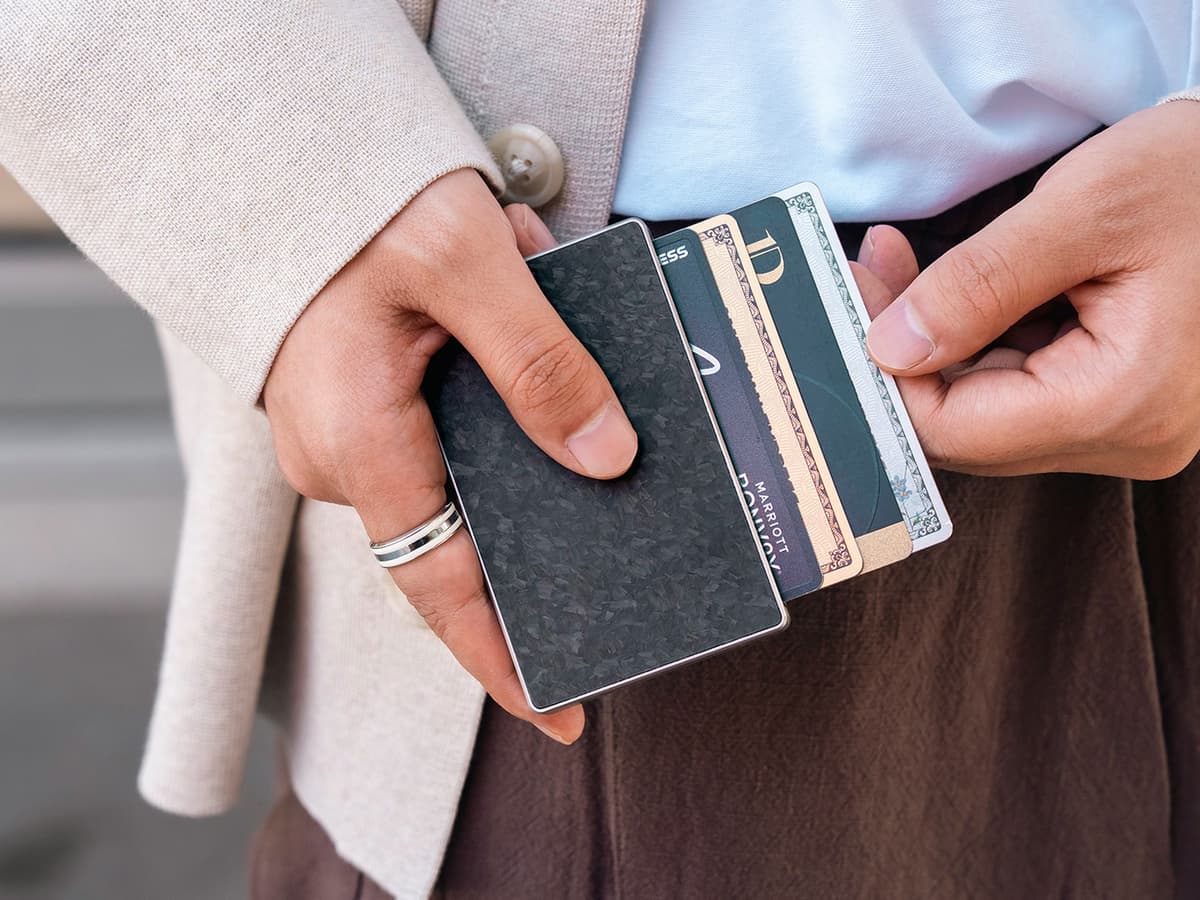 Titaner Verso titanium MagSafe wallet fanning four cards in a staggered stack, held in two hands