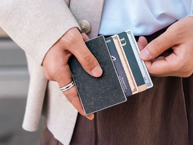 Titaner Verso titanium MagSafe wallet fanning four cards in a staggered stack, held in two hands