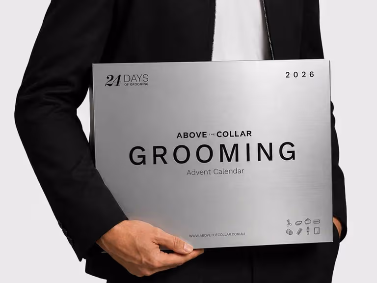 A man in a black jacket holding the brushed silver Above The Collar 24 Days of Grooming advent calendar box for 2026.