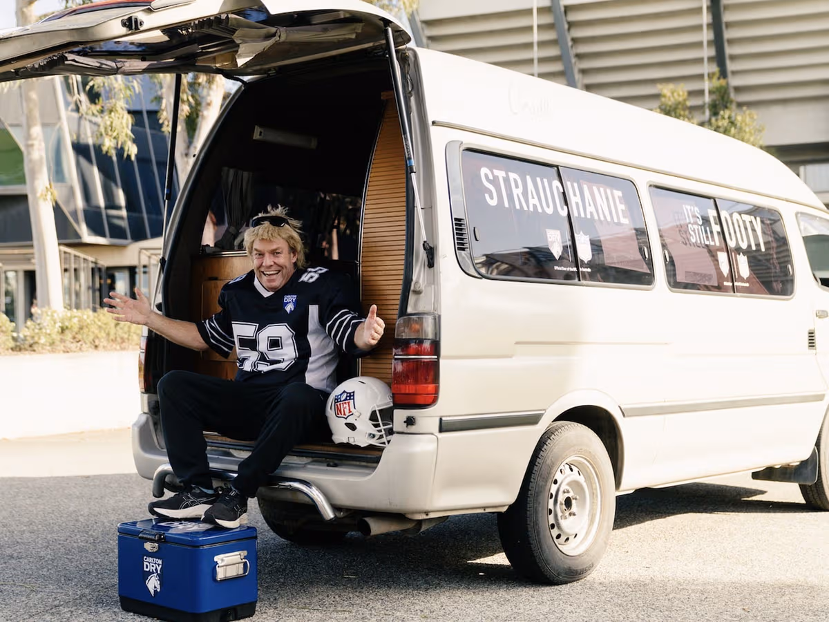 Strauchanie in a number 59 NFL jersey sitting in the back of a van marked It's Still Footy, with an NFL helmet and a Carlton Dry esky
