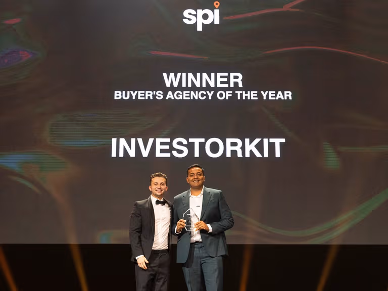 Two men in dinner suits stand on stage beneath a screen announcing InvestorKit as Buyer's Agency of the Year