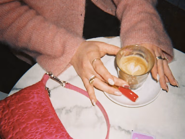 A pink handbag, a coffee and two Moments condom sachets on a marble cafe table