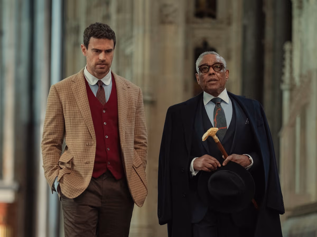 "Two well-dressed men walking together inside a grand, historic stone building with high ceilings and stained glass windows, suggesting a church or cathedral setting."