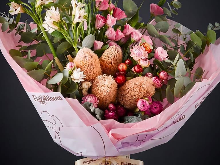 A Fig & Bloom gift spread of fresh flower arrangements, a scented candle and a reed diffuser styled on a table.