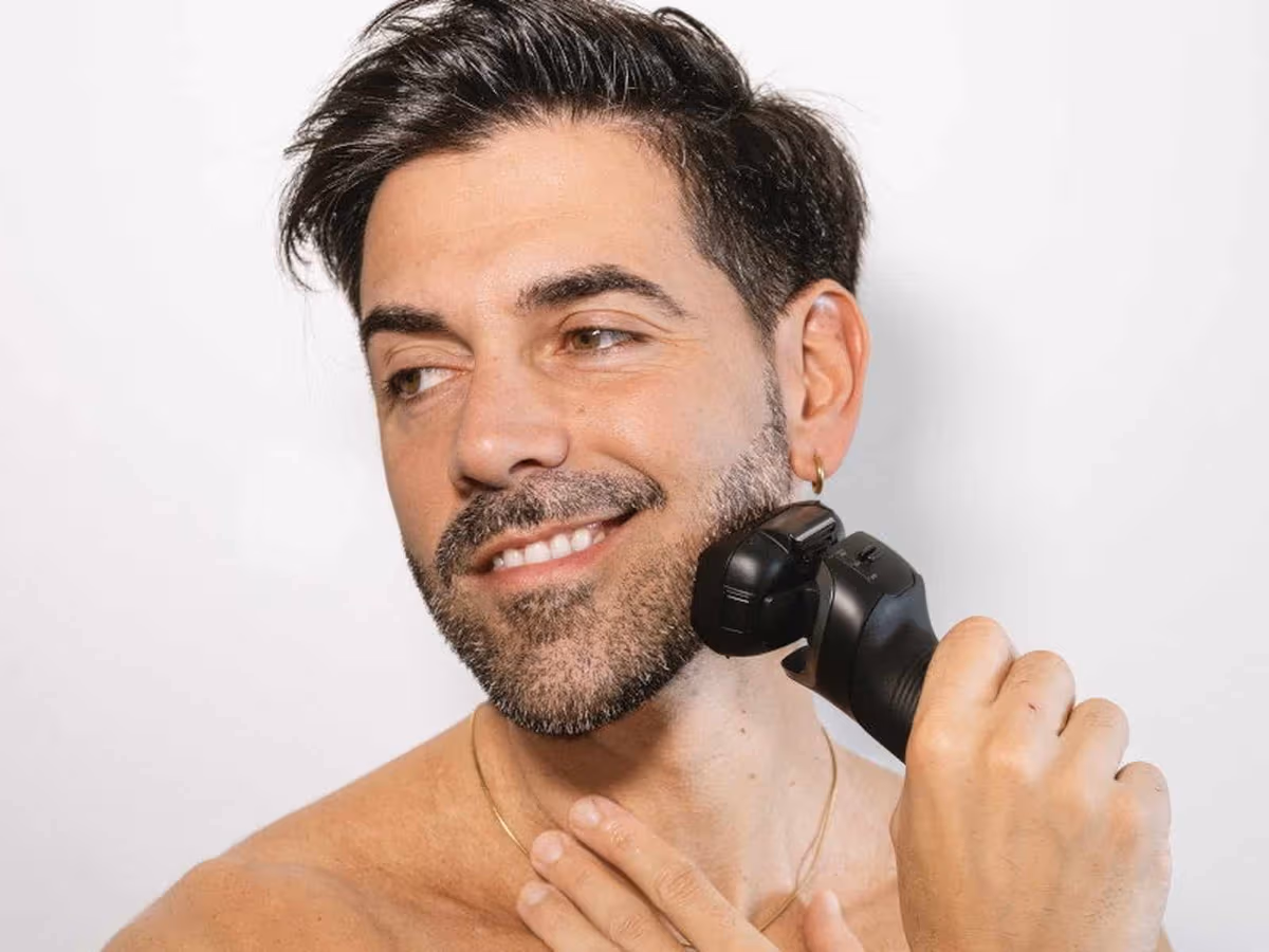 A man with stubble shaving his jawline with the black Panasonic Series 900 PRO ES-L580U electric shaver against a white wall