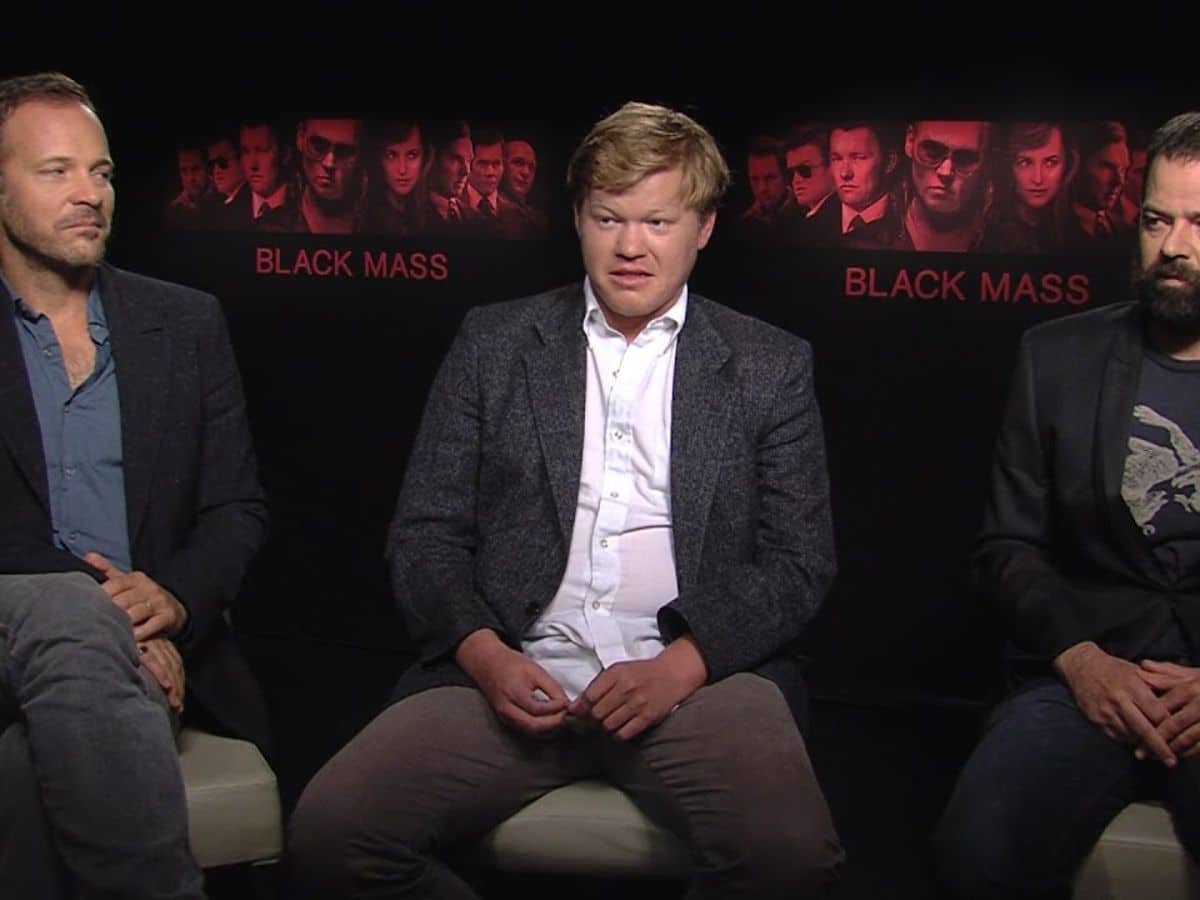 Jesse Plemons in suit at an interview with two other people on his sides
