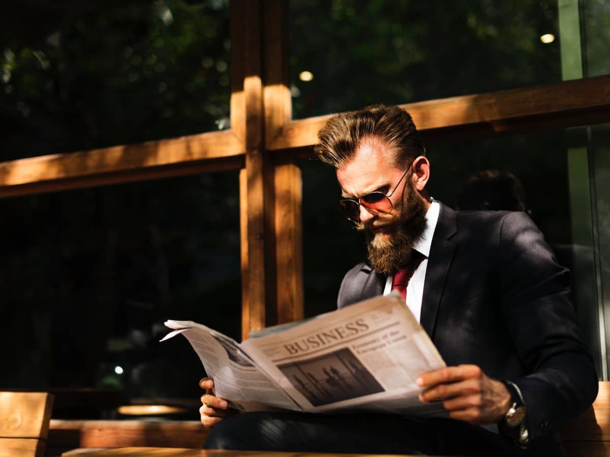 Man in black suit with big beard reading newspaper