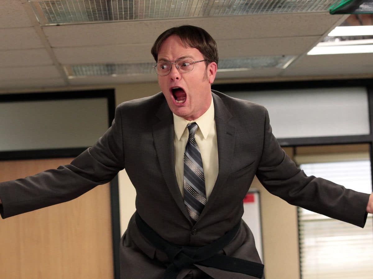 Rainn Wilson as Dwight Schrute standing on a desk and shouting in The Office fire drill episode