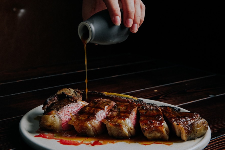 sauce being poured over cut up steak