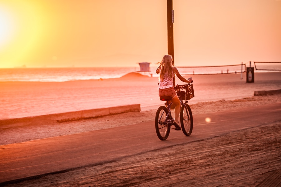 Woman bike riding on huntington beach at sunset