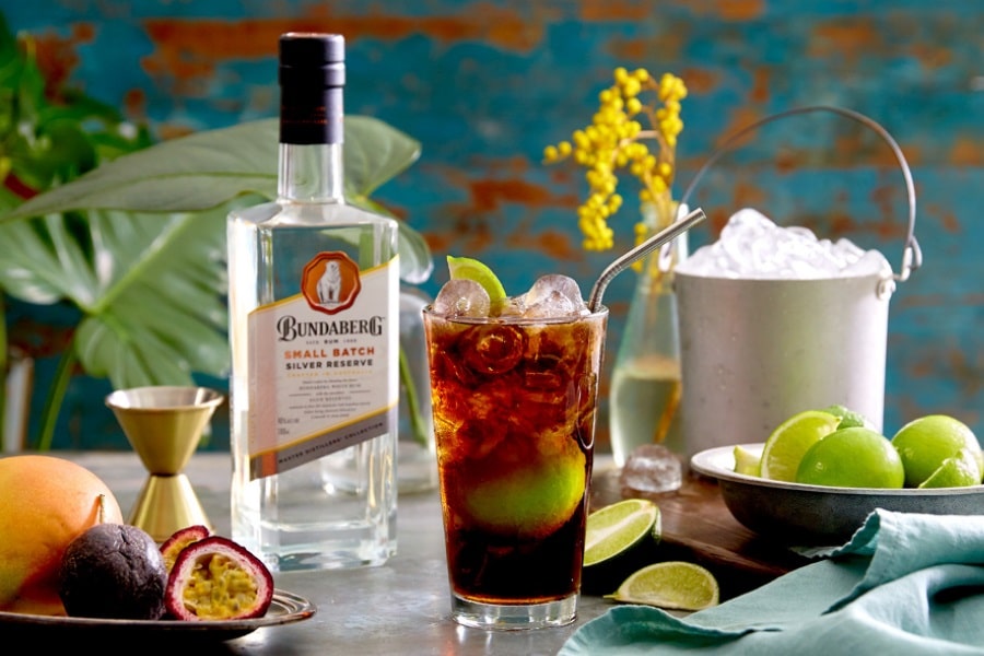 Bundaberg Small Batch Silver Reserve rum bottle with a crafted cocktail, fresh limes, and ice bucket on vibrant vintage backdrop.