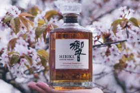 hand holding hibiki whysky bottle near cherry blossoms