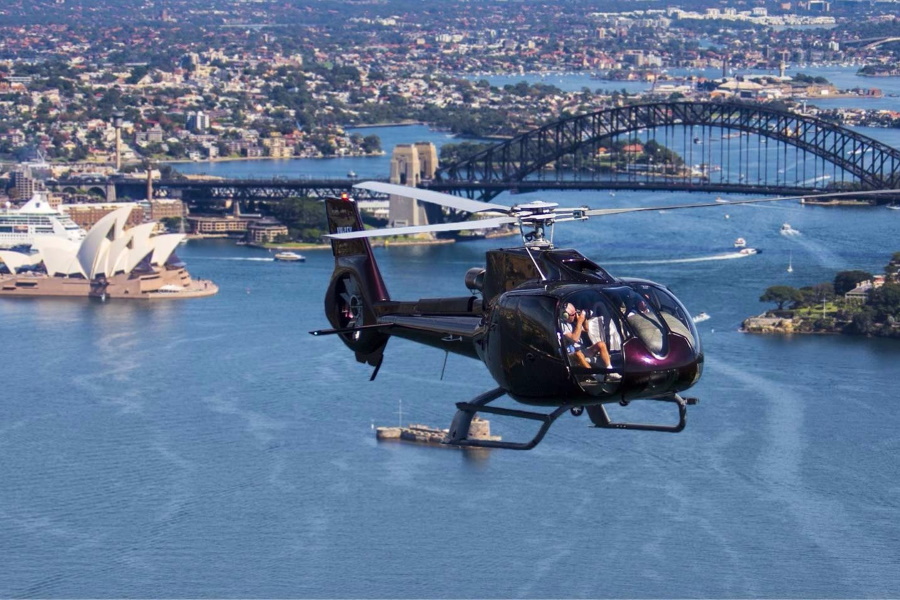 A black helicopter flying over Sydney with Harbour Bridge in background