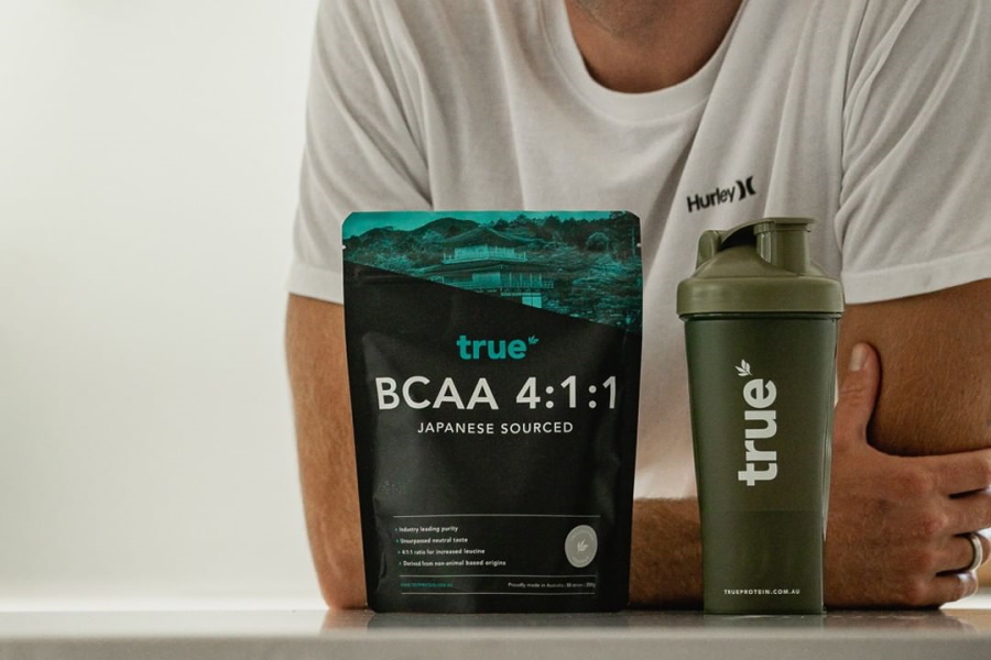 true BCAA 4:1:1 bag and true shaker on a table with a man in background