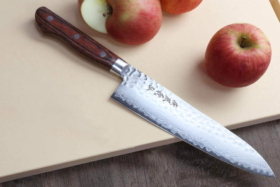 A chef's knife on a wooden board with apples